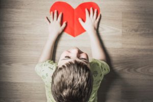 Child with paper red heart on a desk